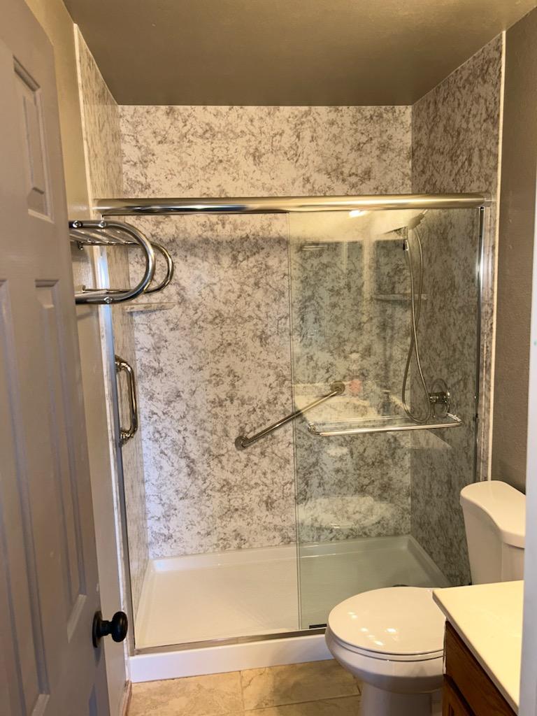 Shower enclosure with curved glass panel, chrome grab bar and handheld.