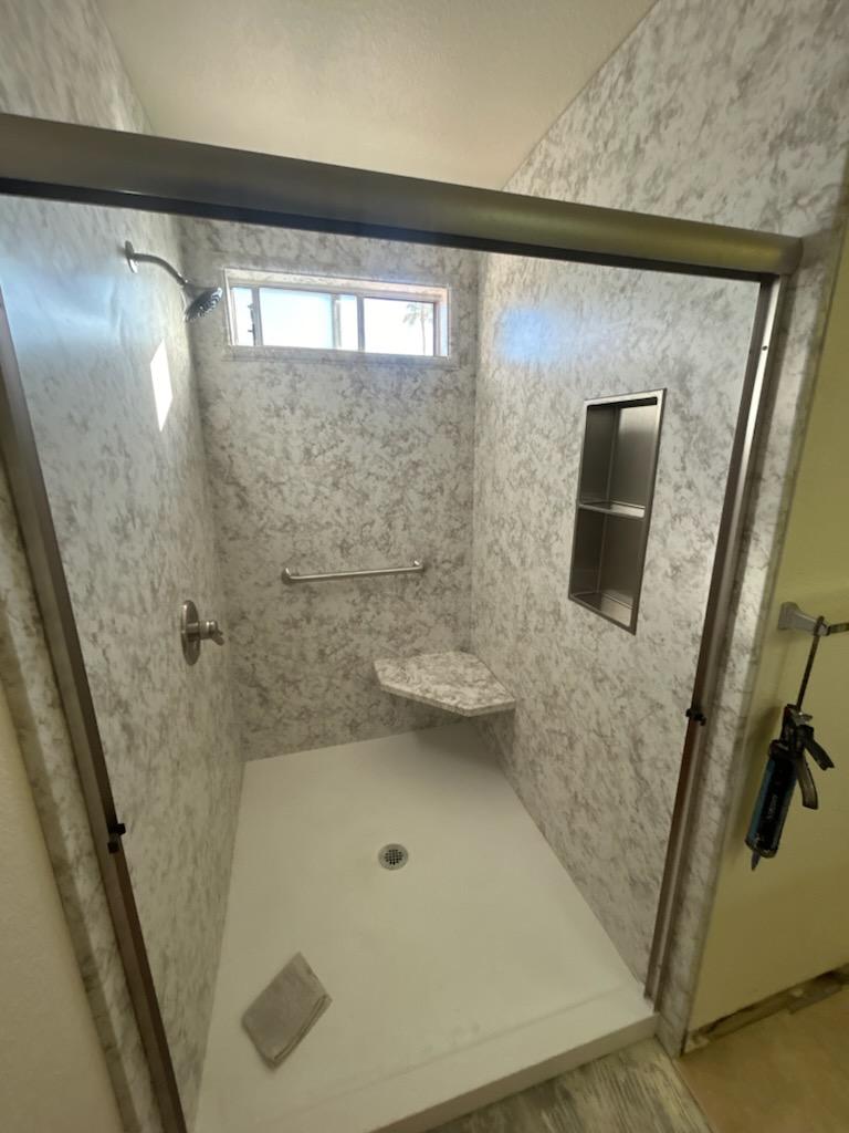 Low-curb corner shower with a built-in seat, recessed niche and a grab bar.